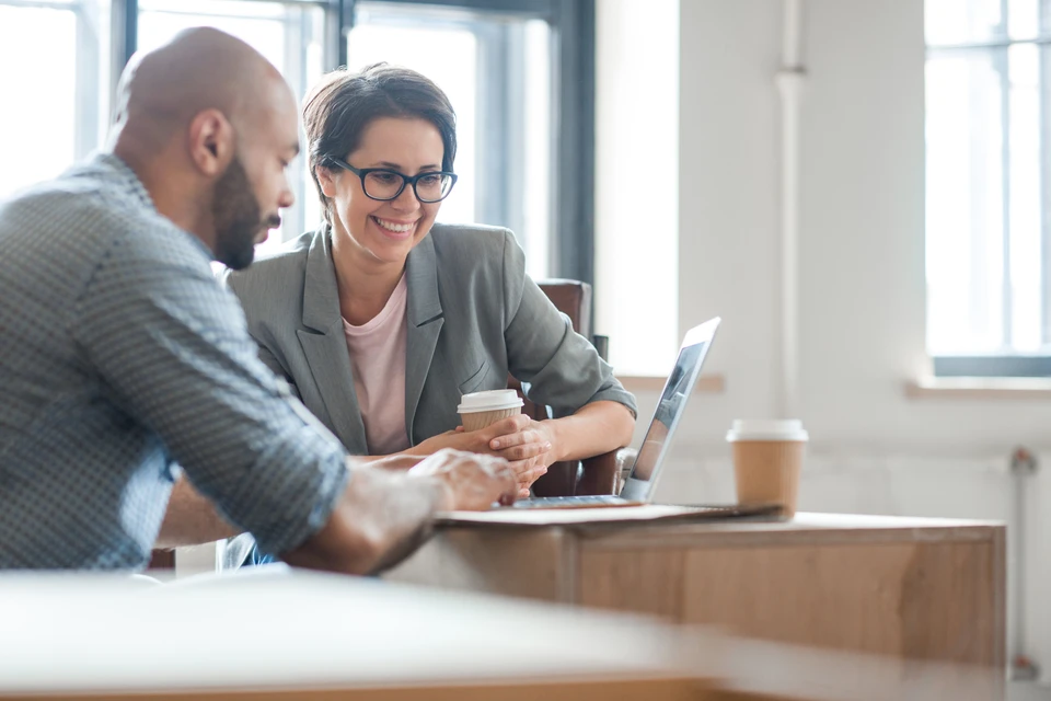Deux professionnels en réunion de travail dans un bureau moderne, homme et femme analysant des données sur ordinateur portable