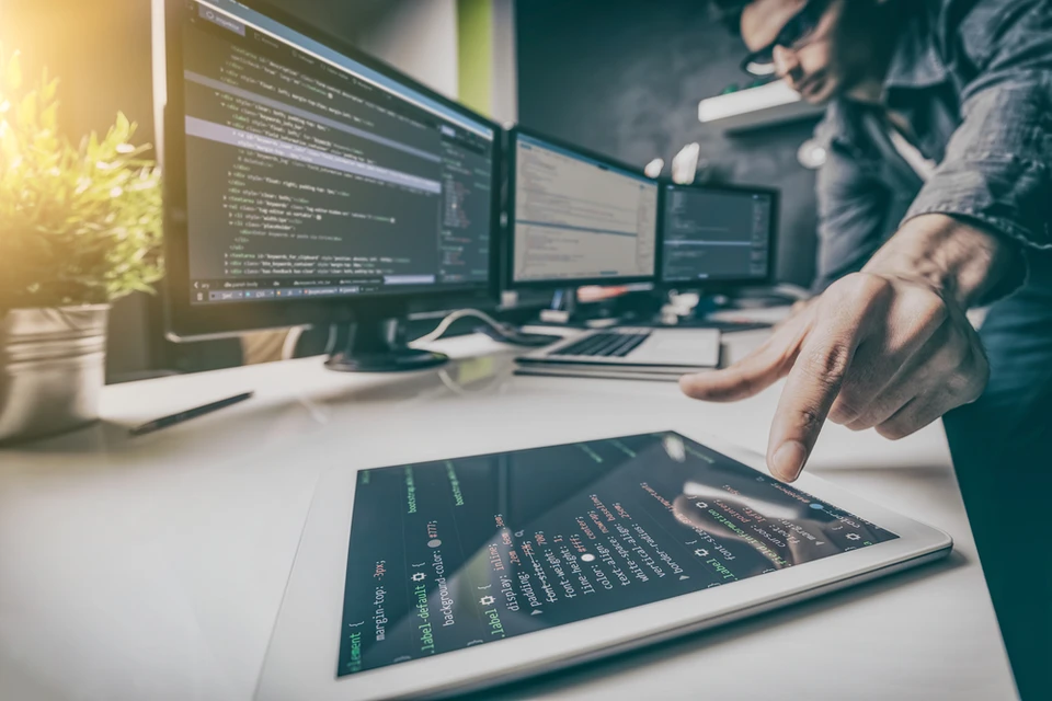 Bureau de développement informatique avec développeur travaillant sur tablette tactile et écrans multiples
