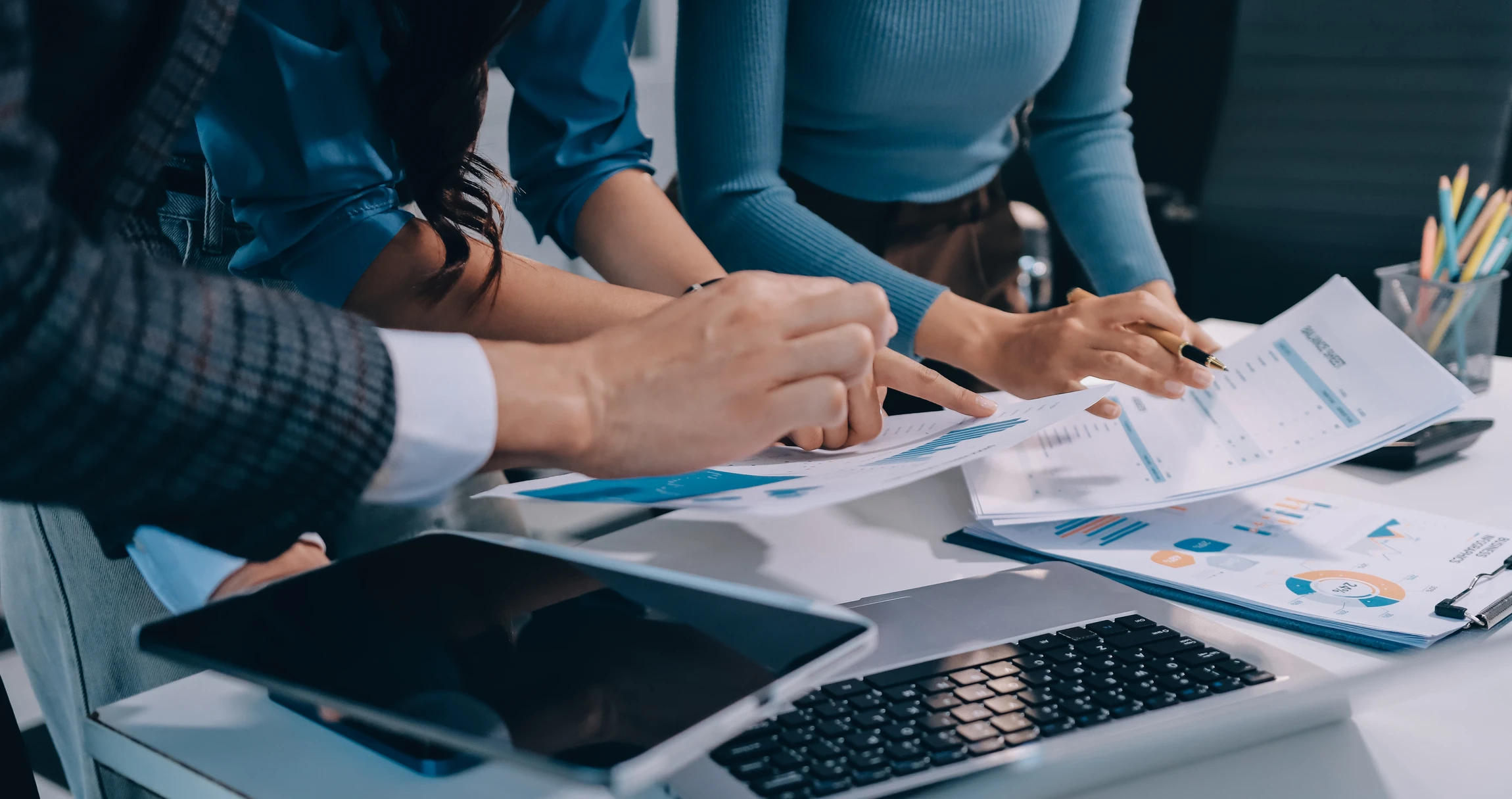 Professionnel en costume travaillant à un bureau avec ordinateur portable, analysant des documents financiers et graphiques imprimés